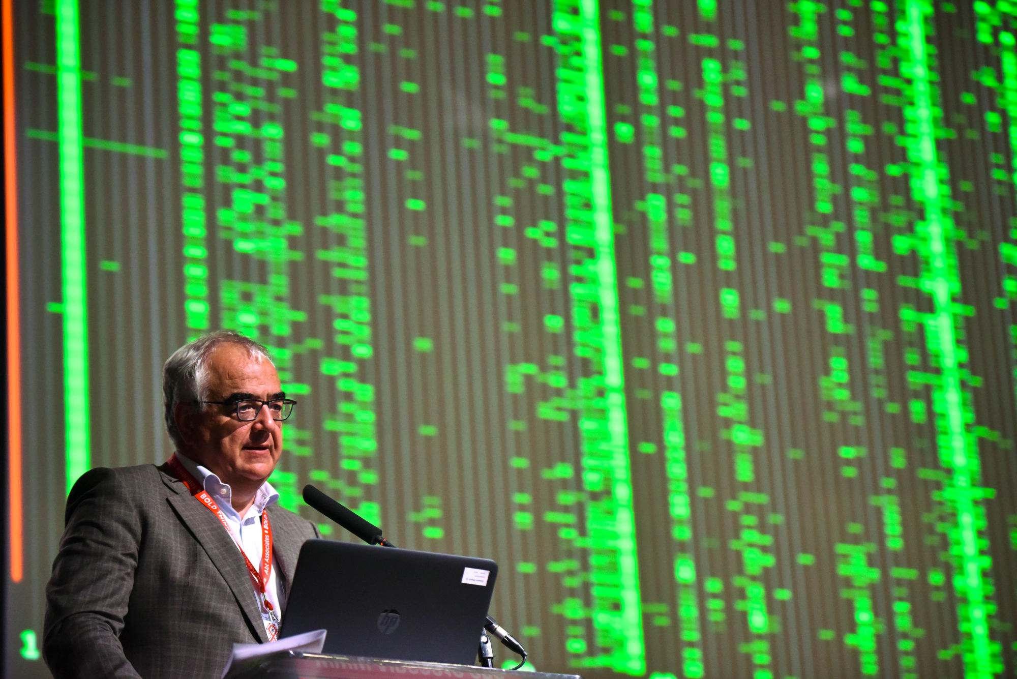 A Johnson & Johnson executive presenting on stage against a large genomic data screen, photographed by Jonathan Burton